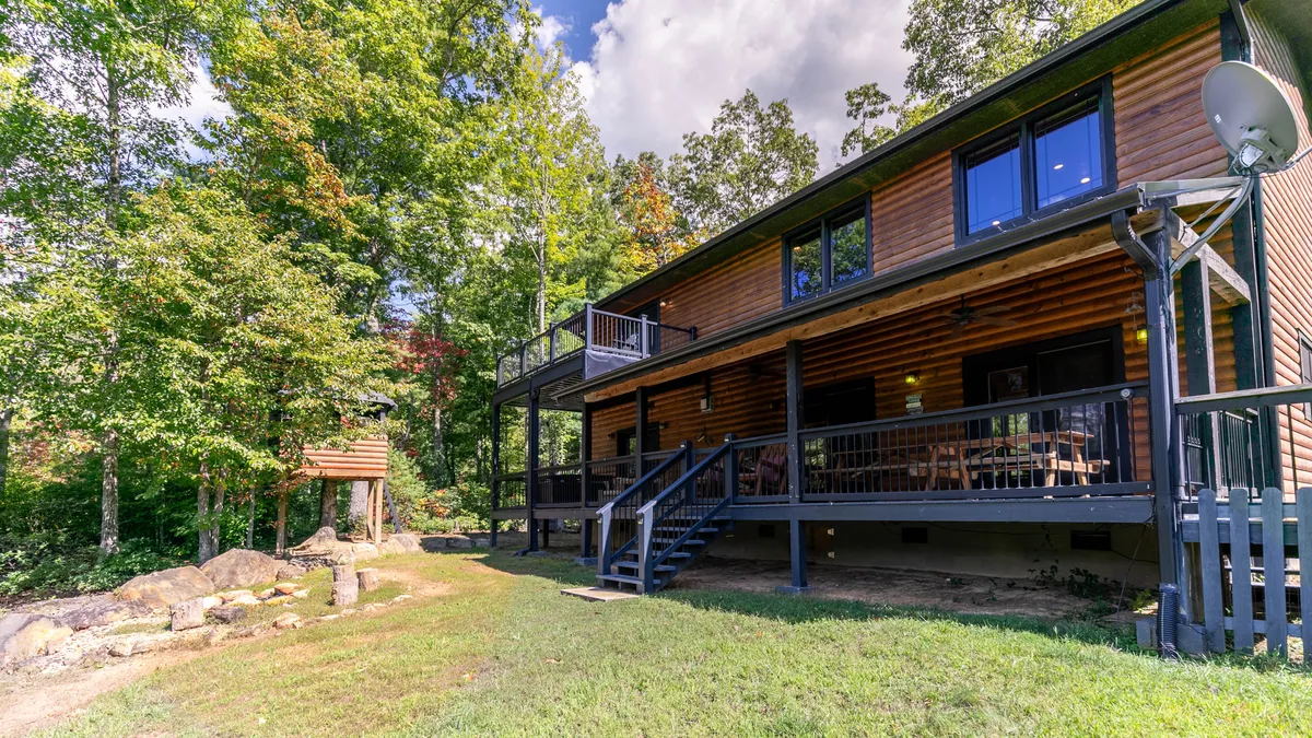 A spacious wooden deck surrounded by lush trees and rugged landscape, featuring an inviting setup perfect for outdoor dining and family gatherings. Natural light bathes the deck, and the tranquil environment hints at the mountain views just beyond.