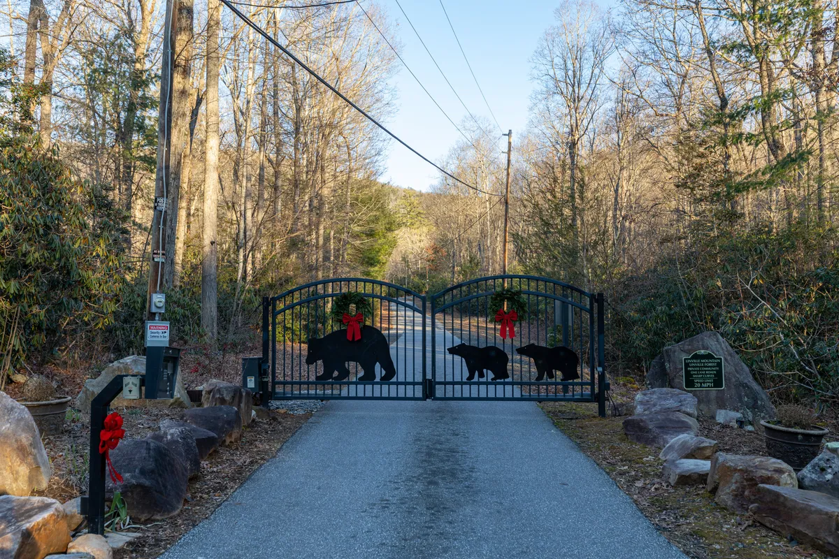 The entrance to the property is marked by an ornate black bear gate adorned with festive red bows, surrounded by natural landscape. The setting hints at both a warm welcome and easy access to the outdoors, with a touch of local character.