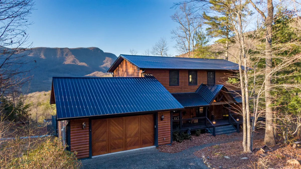 A welcoming cabin exterior with a wooden facade, metal roof, and inviting porch, set among tall trees. The setting radiates warmth and offers glimpses of mountain sunrise and starry evenings.