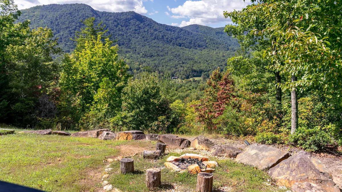 An exterior shot featuring a cozy fire pit surrounded by trees, with distant mountain views visible beyond. The serene setting invites relaxation after a day of exploration, perfect for stargazing or sharing stories around the fire.