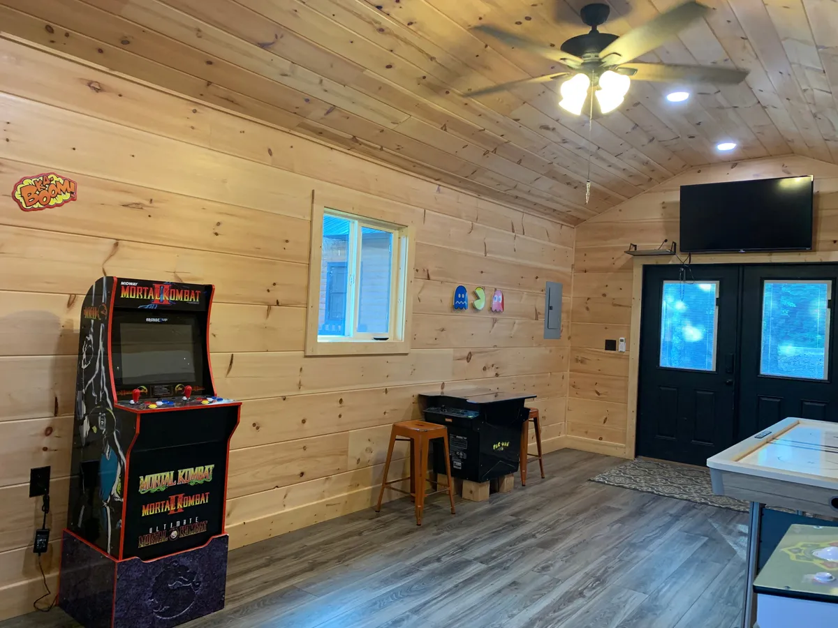 A nostalgic interior scene with an arcade game machine, wooden bar stools, dark double doors, and a television. It radiates a playful, retro vibe, inviting guests to enjoy gaming sessions and relax with friends or family.