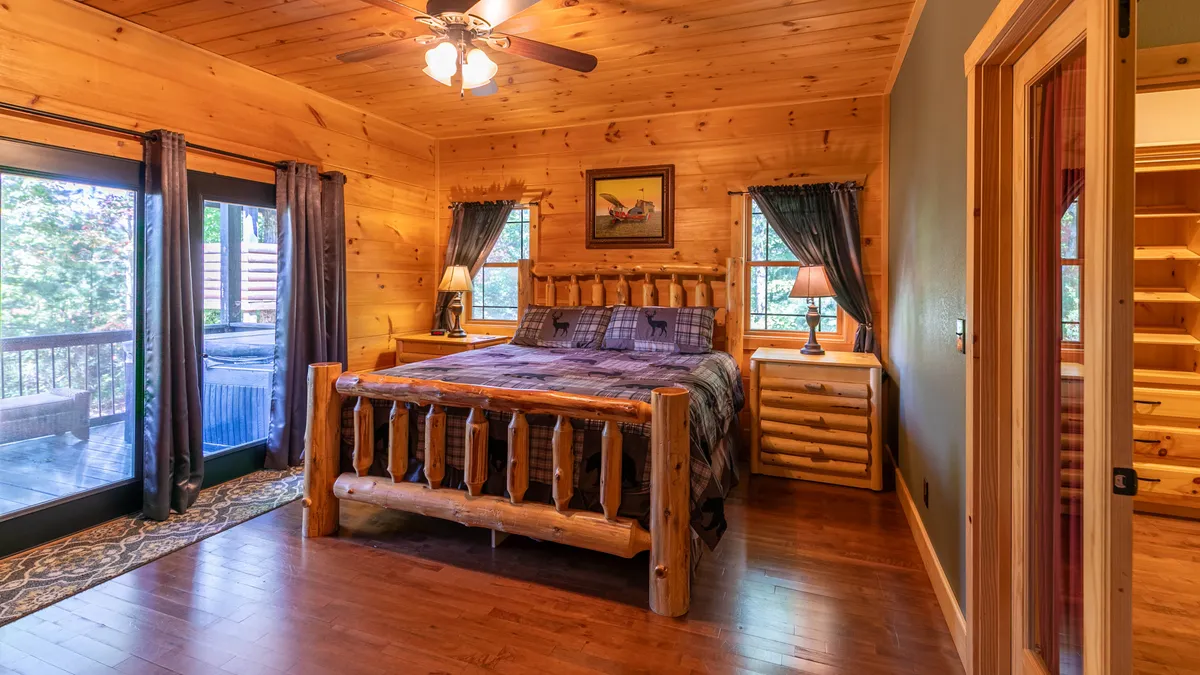 This image presents a log bed flanked by nightstands and lamps, with large windows and curtains allowing in ample natural light. The mood is tranquil and warm, creating a serene and welcoming atmosphere ideal for relaxation.