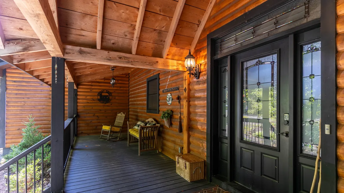 An inviting view of the front porch featuring a wooden rocking chair, outdoor lanterns, and rustic log cabin walls. The welcoming entryway and seating area evoke the idea of relaxing with friends or sharing a drink before or after local adventures.