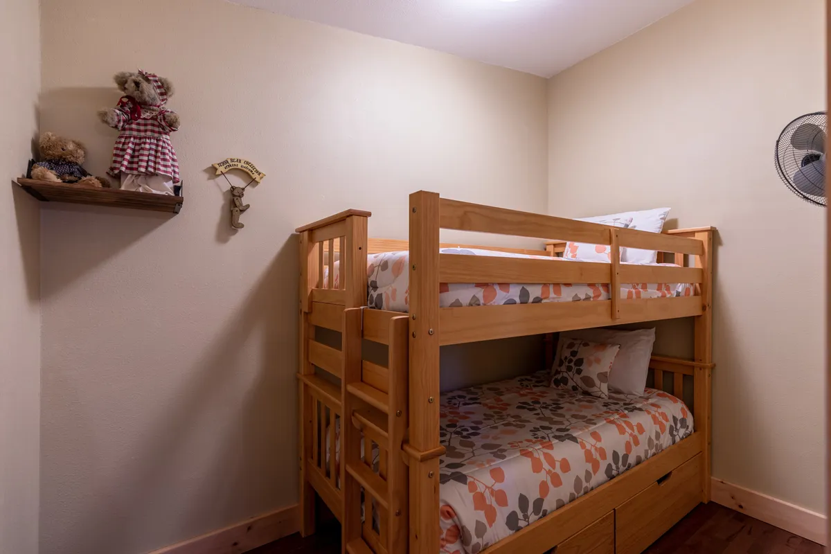 The focal point in this image is a bunk bed adorned with stuffed animals, alongside a decorative wall shelf and a ceiling fan. The ambiance is nostalgic and playful, suggesting a lively space for children or teens.